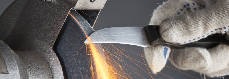Person sharpening a blade with sparks flying, wearing protective gloves.